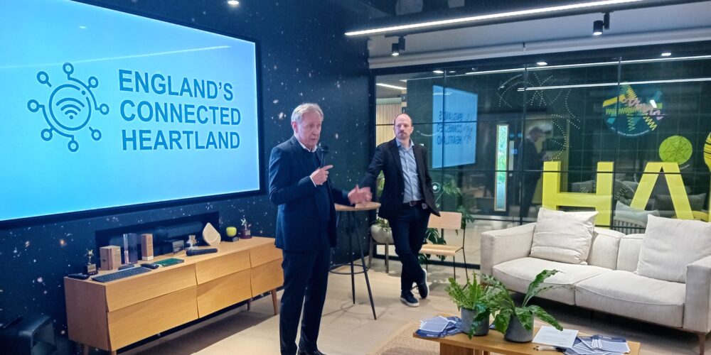 a picture of the two speakers standing in front of a branded screen, speaking to the audience